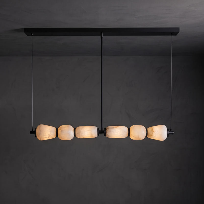 Clérachic linear chandelier with a long black canopy bar, its six lit alabaster pebbles glowing against a dark grey wall.