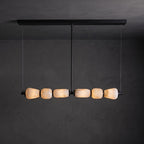 Clérachic linear chandelier with a long black canopy bar, its six lit alabaster pebbles glowing against a dark grey wall.