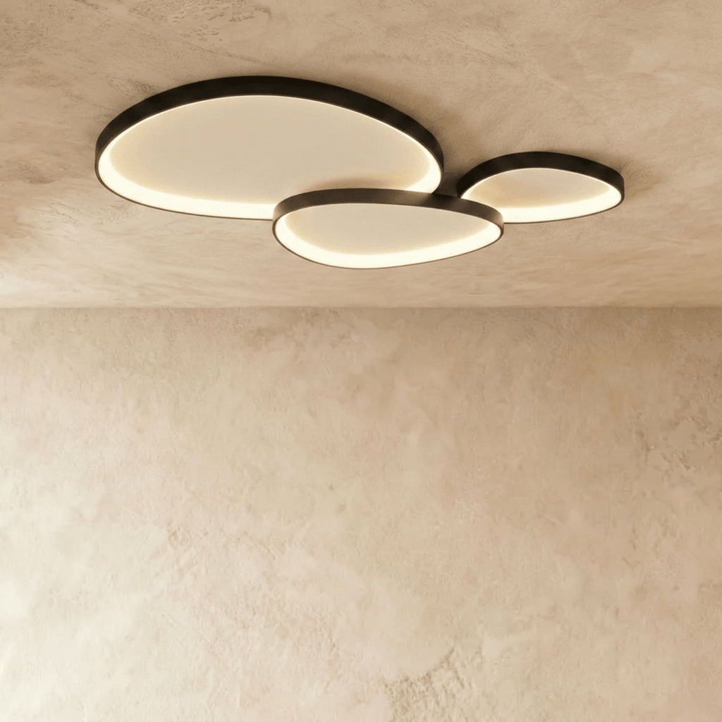 Clérachic cluster of three black pebble-shaped ceiling lights overlapping, each lit warm along its inner rim.