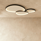 Clérachic cluster of three black pebble-shaped ceiling lights overlapping, each lit warm along its inner rim.