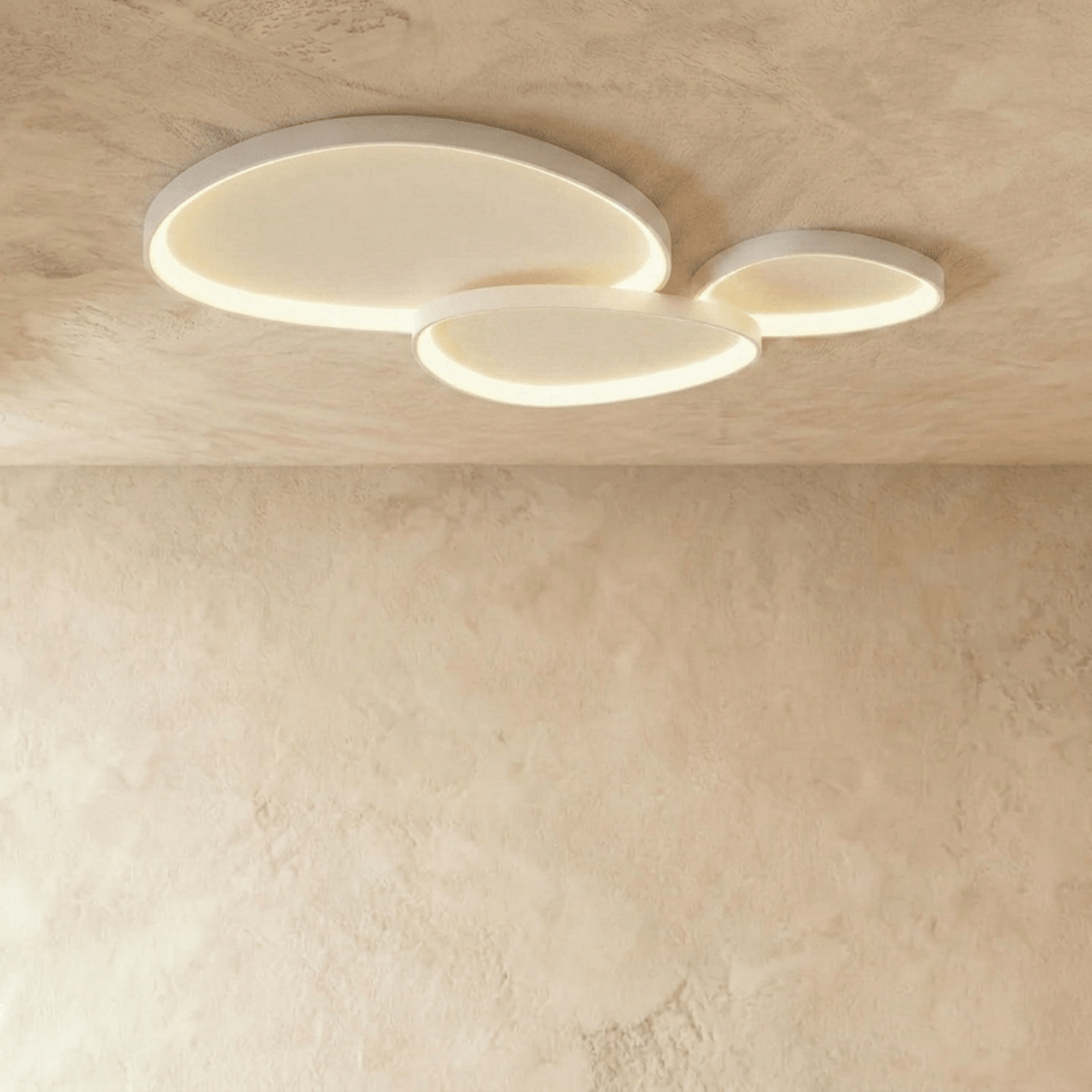 Clérachic group of three white pebble-shaped ceiling lights overlapping, glowing warm on a textured plaster ceiling.