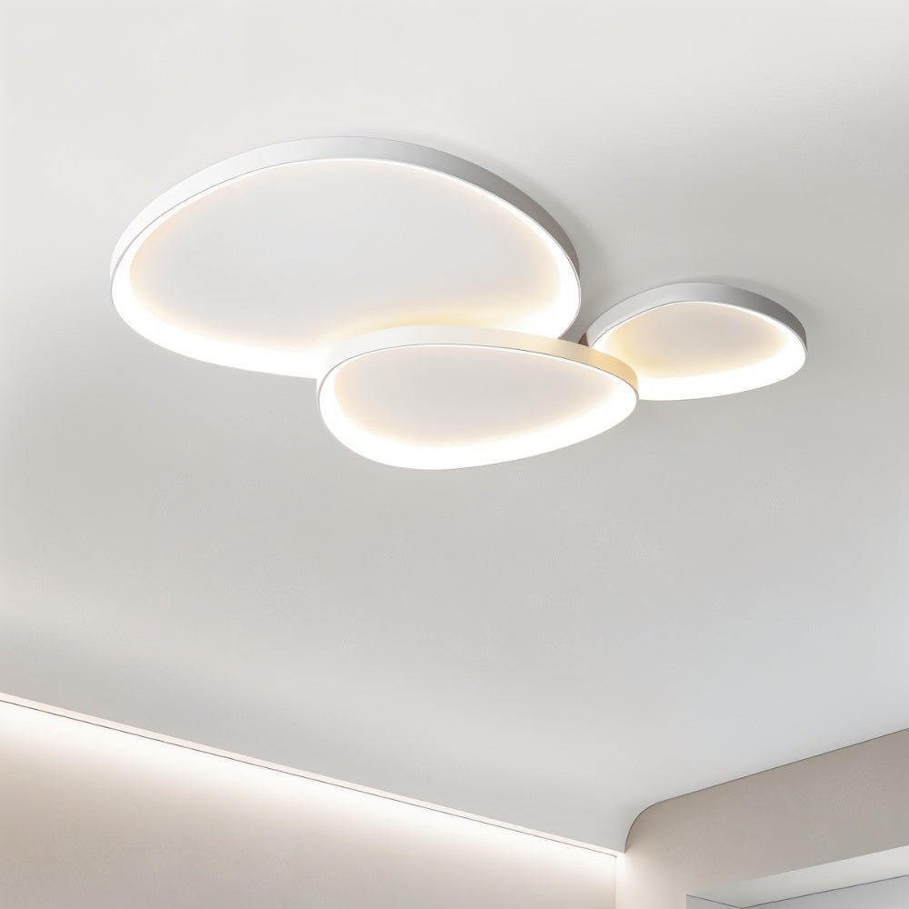 Clérachic three overlapping white pebble ceiling lights lit warm in a bright room with a recessed cove light below.