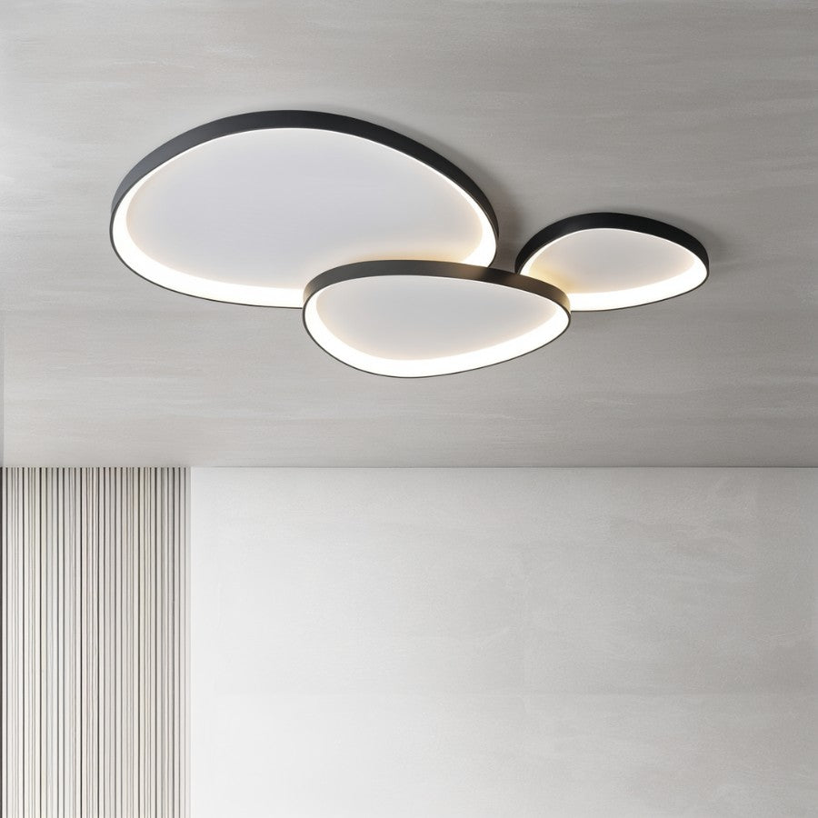 Clérachic three overlapping black pebble ceiling lights lit warm above a grey wall and a ribbed wood panel.