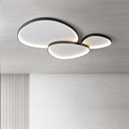 Clérachic three overlapping black pebble ceiling lights lit warm above a grey wall and a ribbed wood panel.