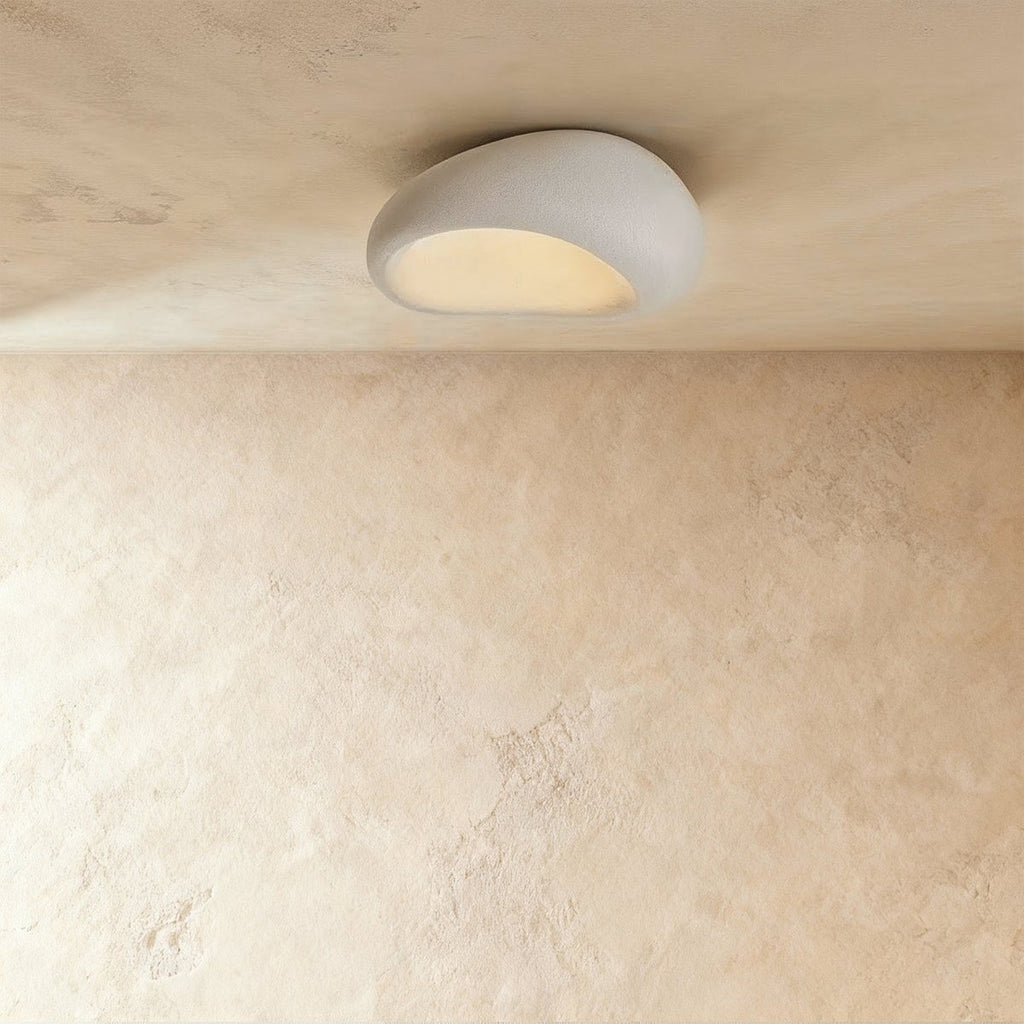Clérachic small white pebble-shaped flush ceiling light with a textured shell, glowing warm beneath a limewashed ceiling.