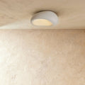 Clérachic small white pebble-shaped flush ceiling light with a textured shell, glowing warm beneath a limewashed ceiling.