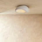 Clérachic small white pebble-shaped flush ceiling light with a textured shell, glowing warm beneath a limewashed ceiling.