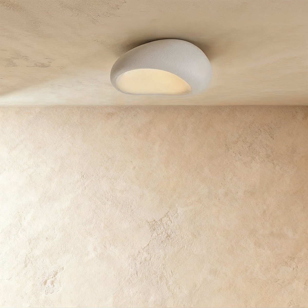 Clérachic small white pebble-shaped flush ceiling light with a textured shell, glowing warm beneath a limewashed ceiling.