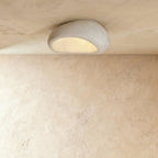 Clérachic pebble-shaped flush ceiling light in a pale speckled cement finish, with warm light glowing from its underside.