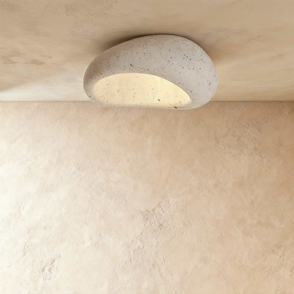 Clérachic mid-size pebble flush ceiling light in speckled cement white, lit warm and mounted on a plaster ceiling.