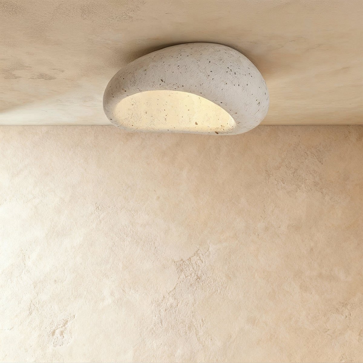 Clérachic mid-size pebble flush ceiling light in speckled cement white, lit warm and mounted on a plaster ceiling.
