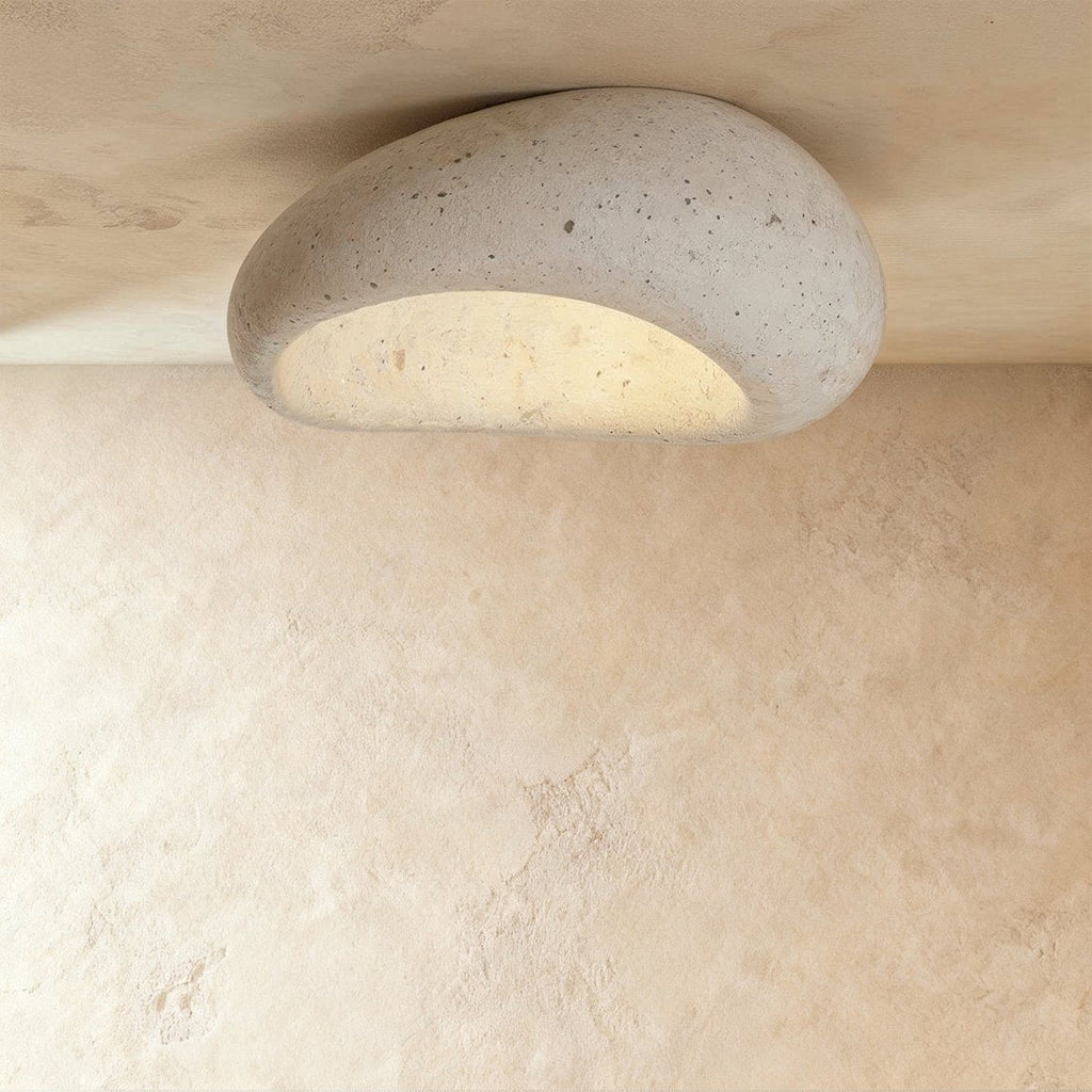 Clérachic large pebble-shaped ceiling light in pale cement white with fine pores, shown close to the ceiling and lit.