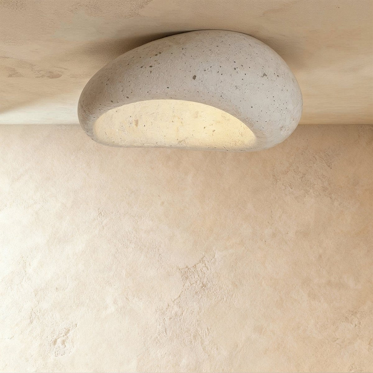 Clérachic large pebble-shaped ceiling light in pale cement white with fine pores, shown close to the ceiling and lit.