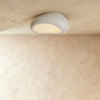 Clérachic matte white pebble flush light with a fine crackled texture, lit warm against a plaster ceiling.