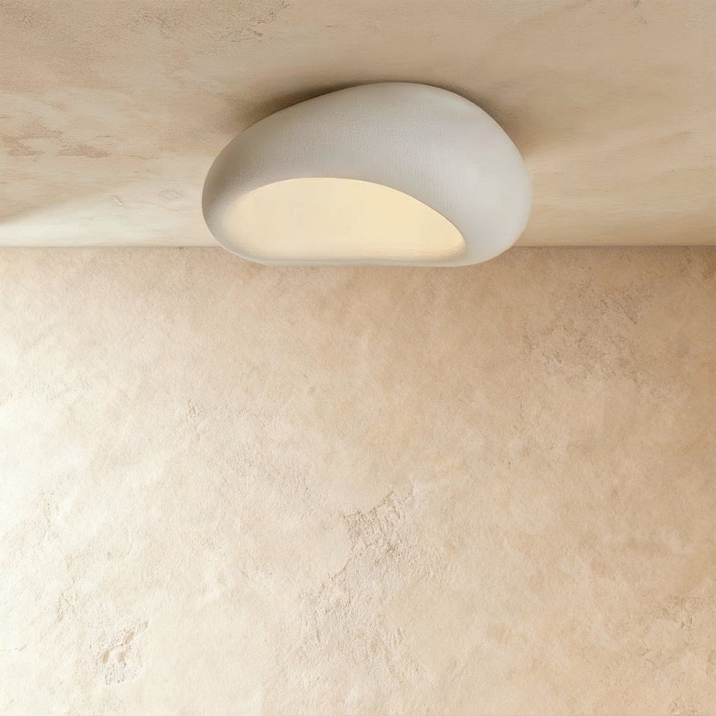 Clérachic white pebble-shaped ceiling light, mid-size, with a frosted opening glowing evenly on a limewashed ceiling.