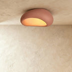 Clérachic larger terracotta pink pebble ceiling light with a fine matte texture and a golden lit opening.