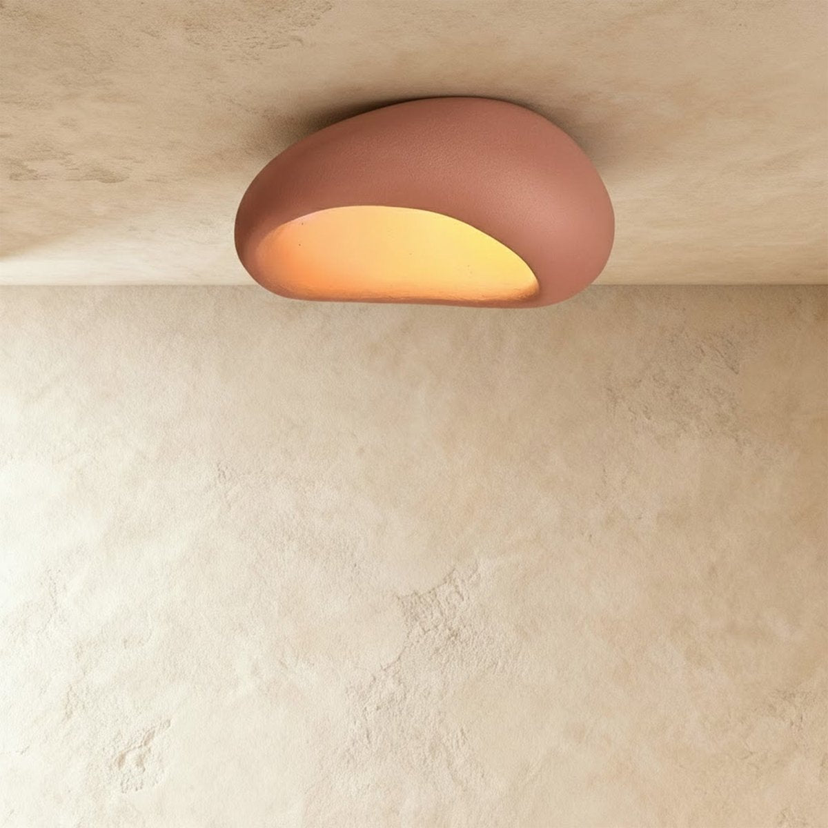 Clérachic larger terracotta pink pebble ceiling light with a fine matte texture and a golden lit opening.