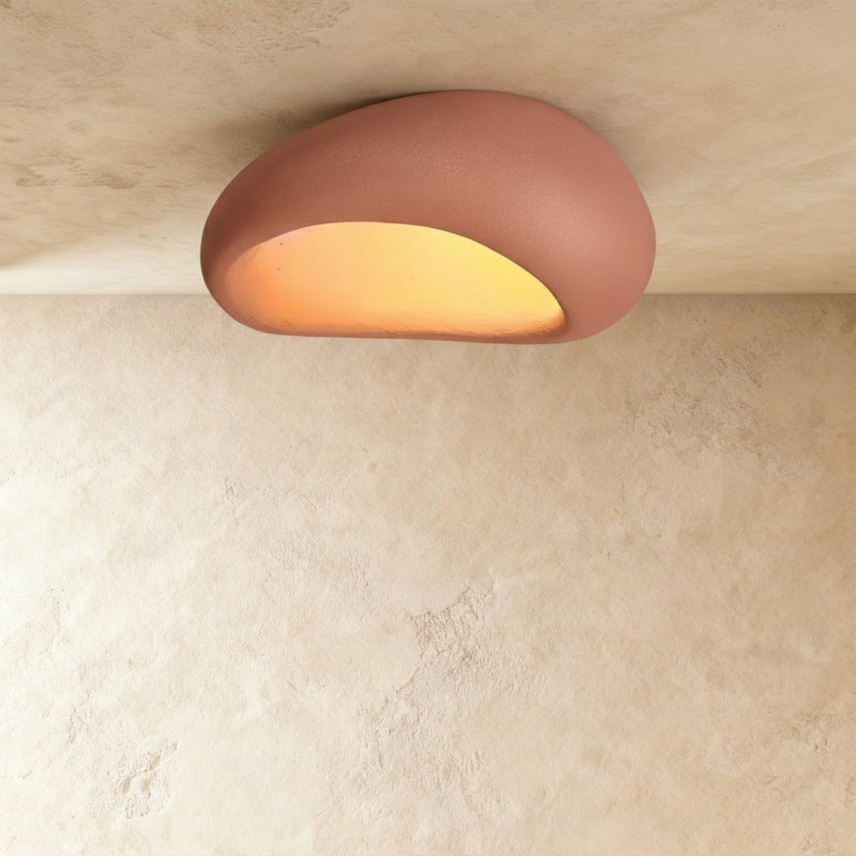 Clérachic wide terracotta pink pebble flush light with a curved shell and a warm amber opening against plaster.