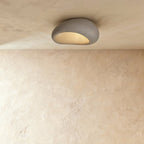 Clérachic small grey pebble-shaped flush ceiling light with a mottled matte shell and a warm glow beneath.