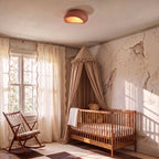 Clérachic terracotta pink pebble flush ceiling light in a nursery with a gingham canopy, wooden cot and rocking chair.