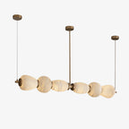 The Clérachic Pebble linear chandelier lit on white, stone shapes graduating along the bar.