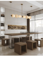 The Clérachic Pebble chandelier over a long communal table with timber block seating.