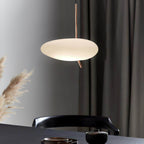 Clérachic pendant light glowing above a dark dining table set with small cups, framed by pampas grass and a curtain.