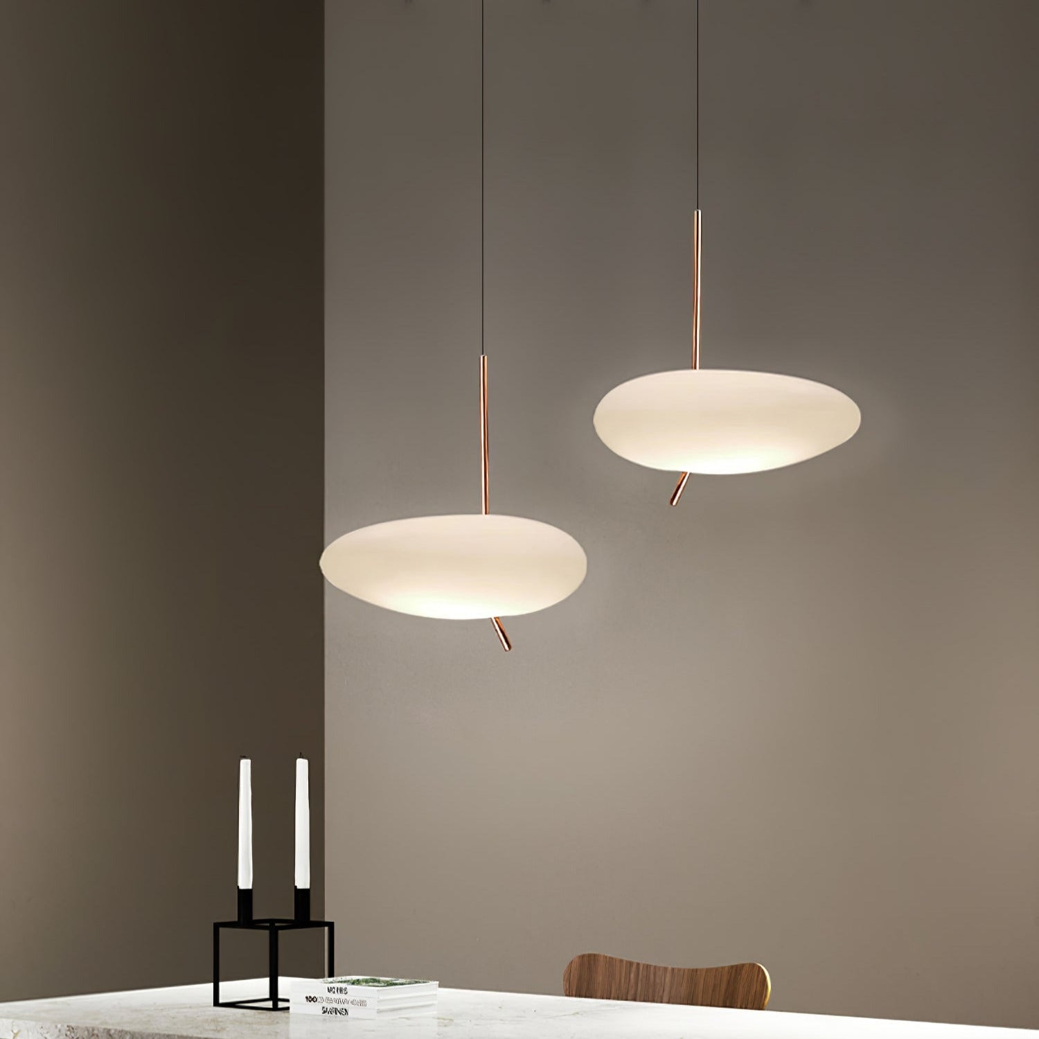 Two Clérachic pebble pendants lit at staggered heights near a candle holder and stacked books in a moody dark room.
