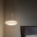 Clérachic pebble pendant lit beside a black leather chair and a gray textured cushion in a dim charcoal room.