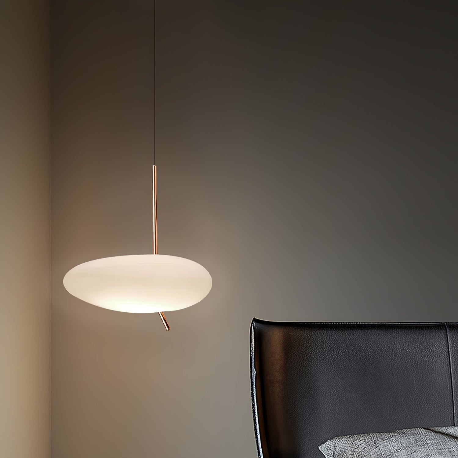Clérachic pebble pendant lit beside a black leather chair and a gray textured cushion in a dim charcoal room.