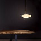 A hand reaches toward the glowing Clérachic pendant, set against a cream wall with classic crown molding.