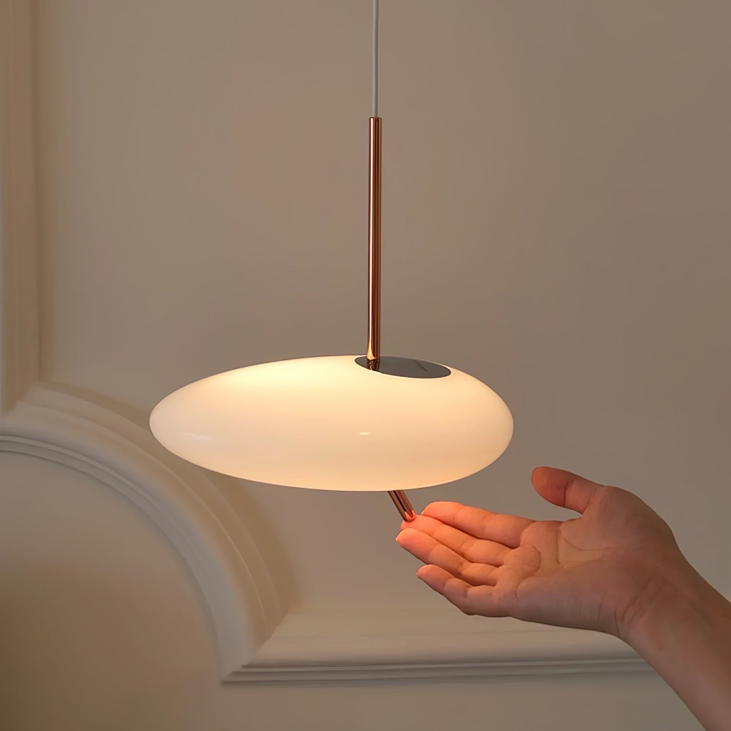 Clérachic pebble pendant glowing above an open palm reaching up from below, set against a near-black backdrop.