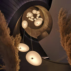 The Clérachic pendant's mounting hardware shown up close, framed by stacked books and a vase of pink roses.