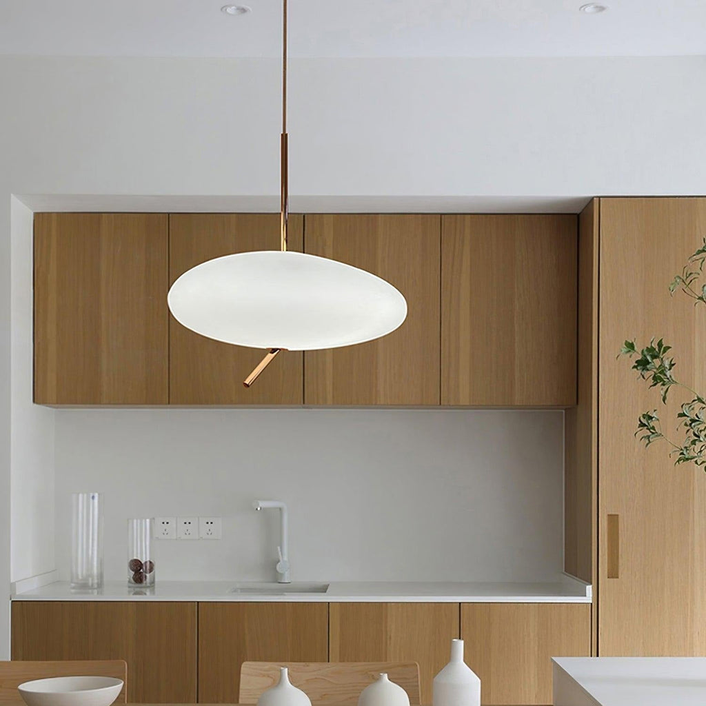 A single Clérachic pendant lights a wood-cabinet kitchen counter beside a stainless sink and small vases.