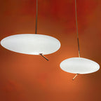 Two Clérachic pebble pendants glow against a deep orange wall, their rose gold stems catching the light.