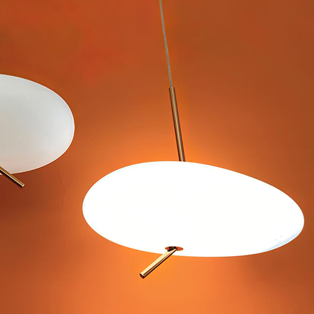 Close-up of a Clérachic pendant's frosted shade and stem against a warm orange wall, another shade just visible.