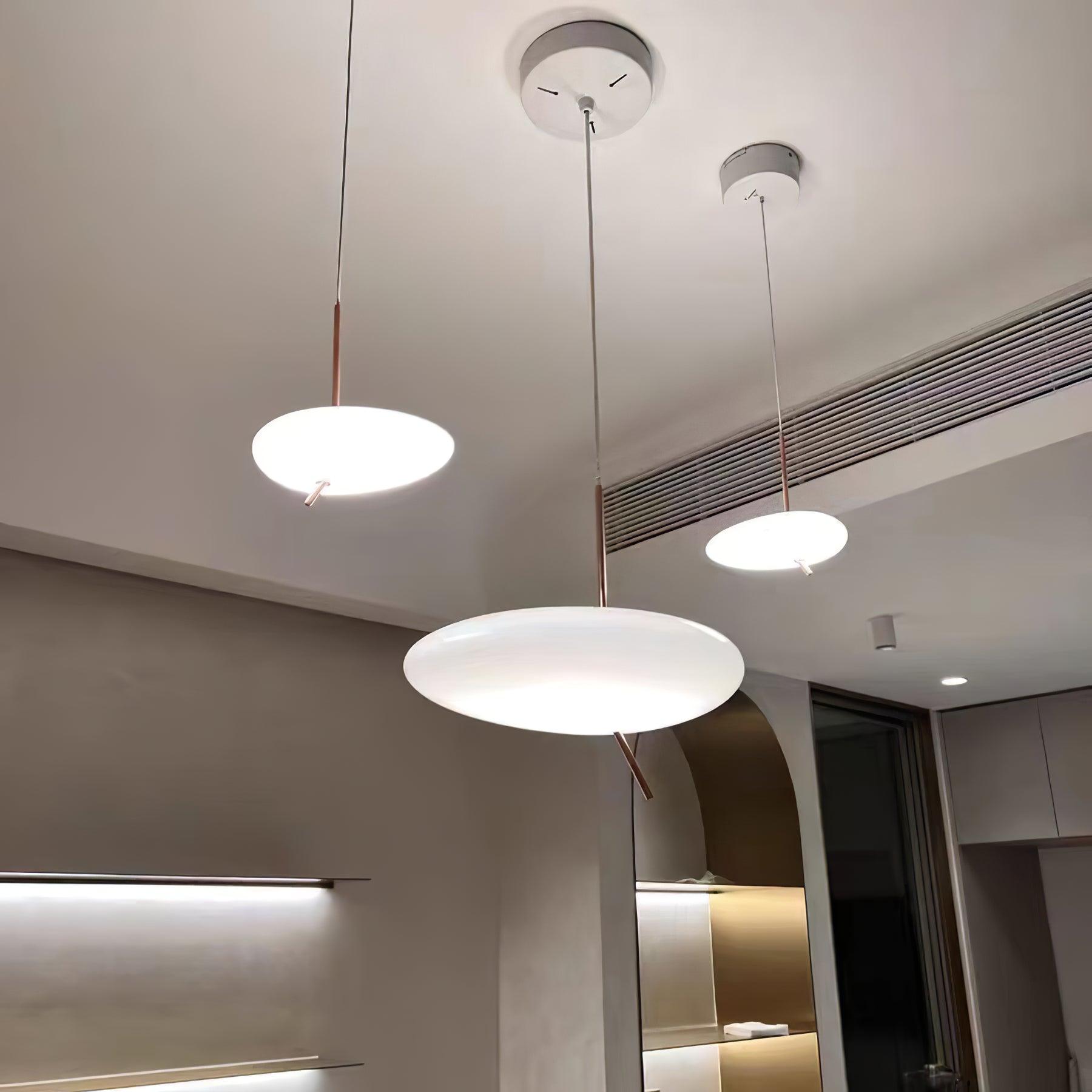 Three Clérachic pebble pendants at staggered heights light a kitchen and living space beneath an arched doorway.