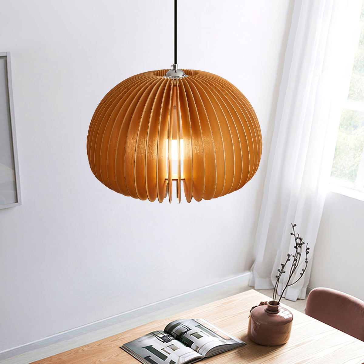 A Clérachic natural wood pendant hung in a corner by a window with a sheer curtain, above a wooden table with a magazine and a vase.