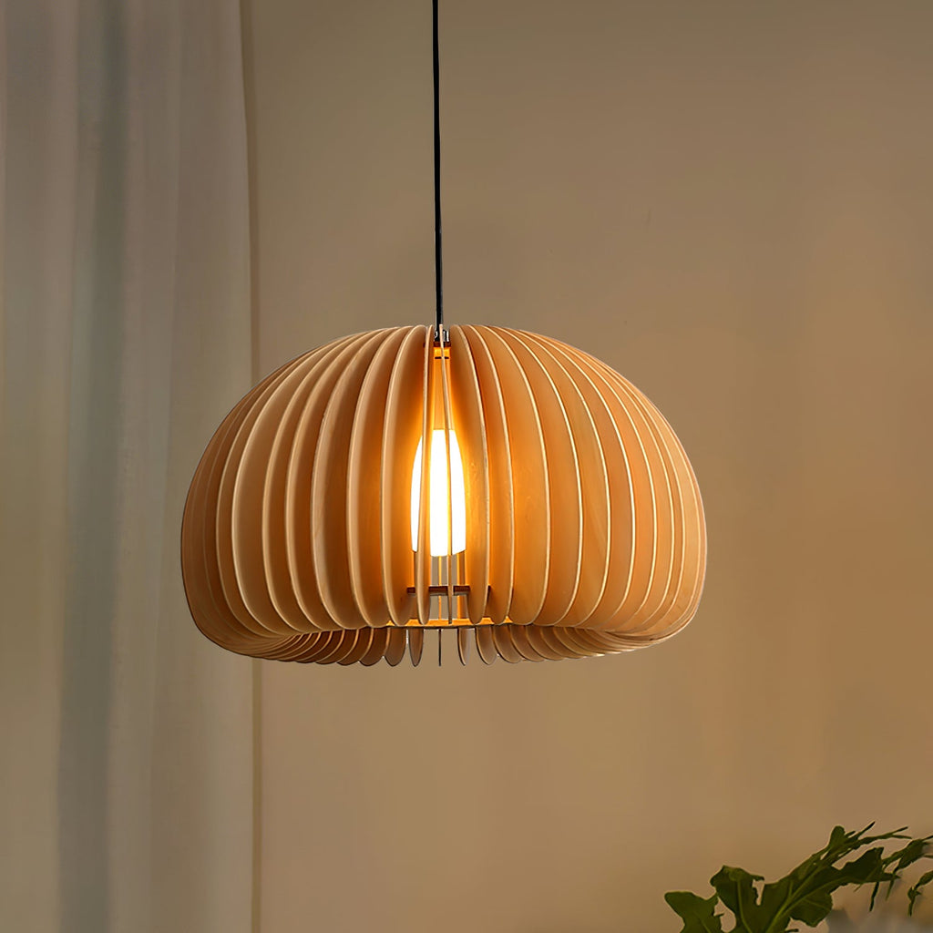 Clérachic wood slat pendant glowing against a warm tan wall, with a curtain on the left and a leaf at the edge of the frame.