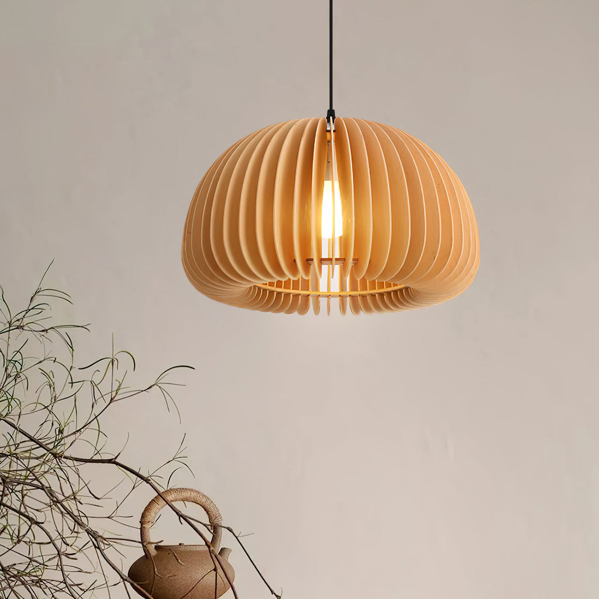 Clérachic wood pendant seen from slightly below, its slats curving into a rounded shade, with dry twigs and a teapot in the corner.