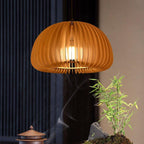 Clérachic wooden pendant glowing against dark curtains, with a wisp of incense smoke and a small bamboo plant below.