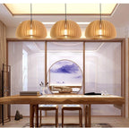Three Clérachic slatted pendants in a row above a long wooden desk, in a calm study with a round window and a mountain painting.