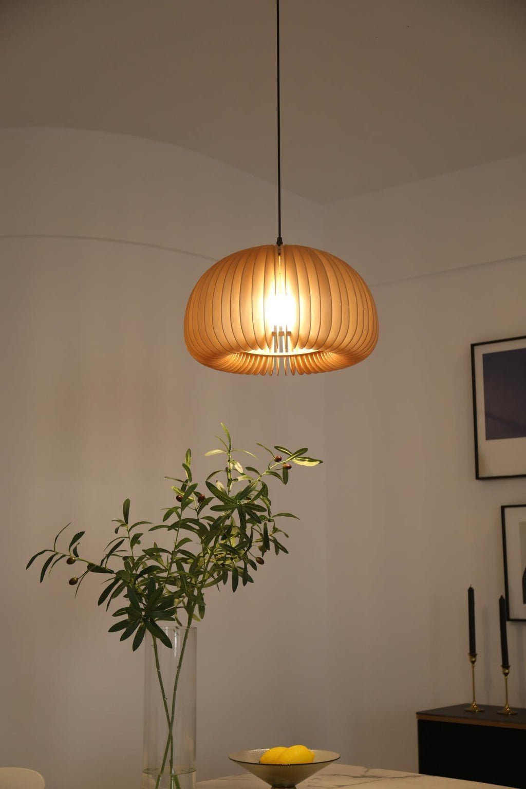 Clérachic slat pendant above a dining corner with a vase of olive branches, a dish of lemons and framed prints on the wall.