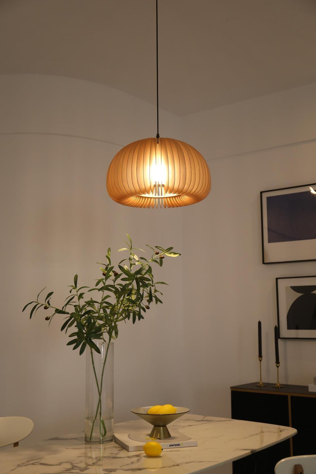 Lit Clérachic slatted pendant above a marble-topped table with a green stem in a glass vase and a dish of lemons.