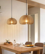 Two Clérachic slatted pendants of different sizes hung over a wooden dining table with a woven tray and a water bottle.