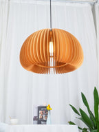 Clérachic wood pendant lit in front of billowing white curtains, with a plant, a small book and a cup on a table below.