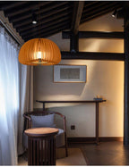 Clérachic slatted pendant glowing amber in a dark-beamed room with a pale wall, a console table and a carved wooden chair.