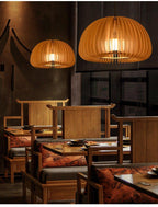 Two Clérachic wood slat pendants of different sizes lit over a restaurant booth with wooden chairs and rust-coloured cushions.