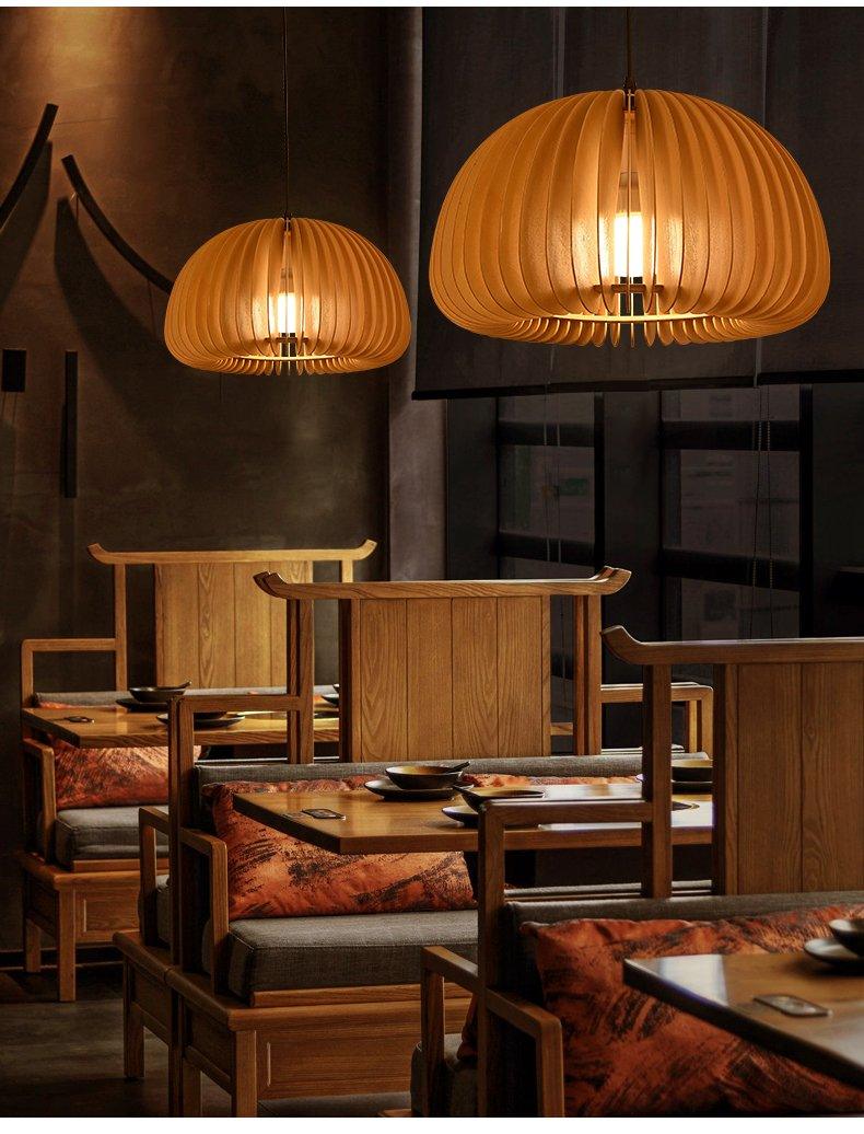 Two Clérachic wood slat pendants of different sizes lit over a restaurant booth with wooden chairs and rust-coloured cushions.