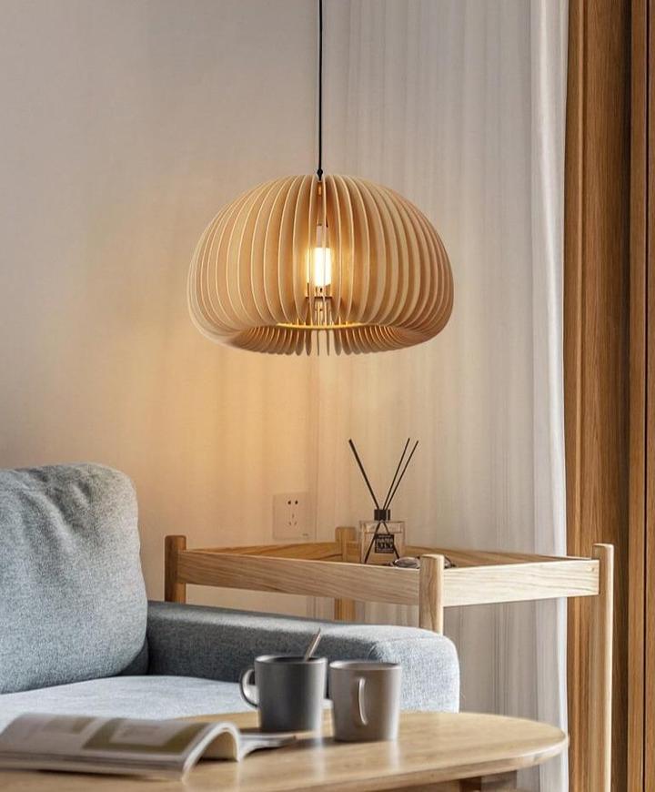 A Clérachic slatted pendant lit beside a grey sofa, a round coffee table and a reed diffuser, with a tall curtain at the side.